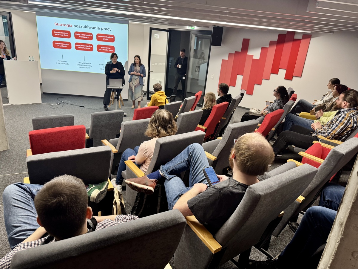 A presentation in the auditorium during the Job Fair. Marta Pigla and a Polish Sign Language interpreter speak in front of a screen showing the slide “Job search strategy” (in Polish). Participants are seated and listening.